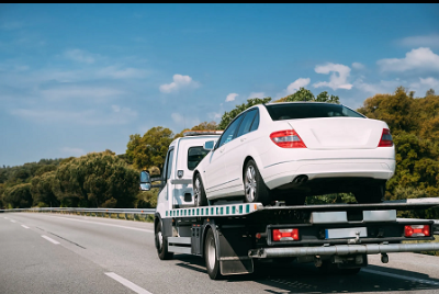 Flatbed tow truck transporting a white sedan
